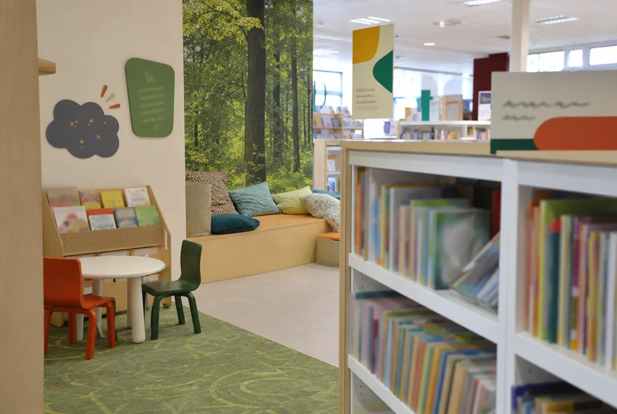Kącik dziecięcy w bibliotece z fototapetą i oznaczeniami regałów