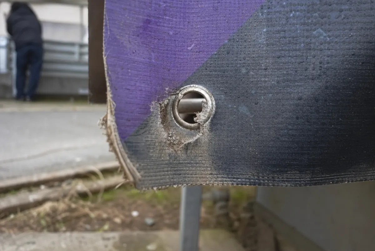 Zniszczona krawędź banera z wyrwanym oczkiem i wyblakłym kolorem