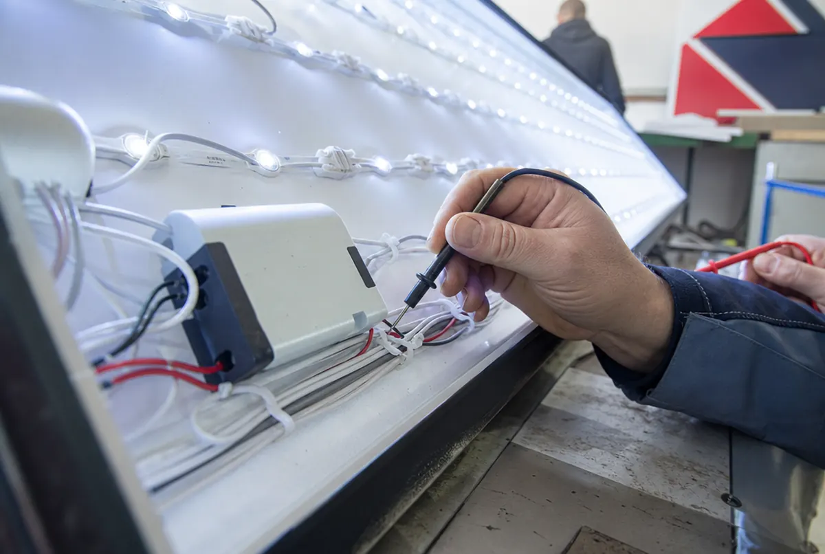 Moduły LED i zasilacz w kasetonie sprawdzane miernikiem przez technika
