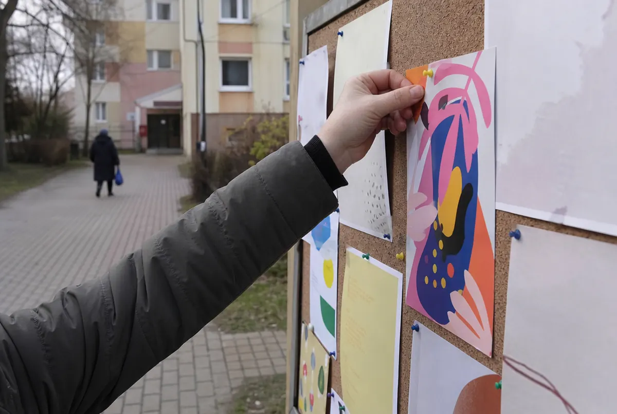 Dłoń przypina ulotkę do tablicy ogłoszeń na osiedlu