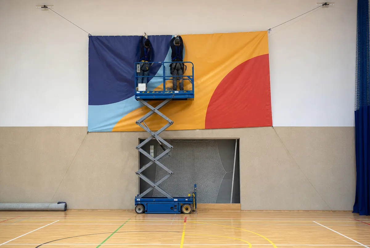 Monterzy na podnośniku wieszają baner na ścianie hali