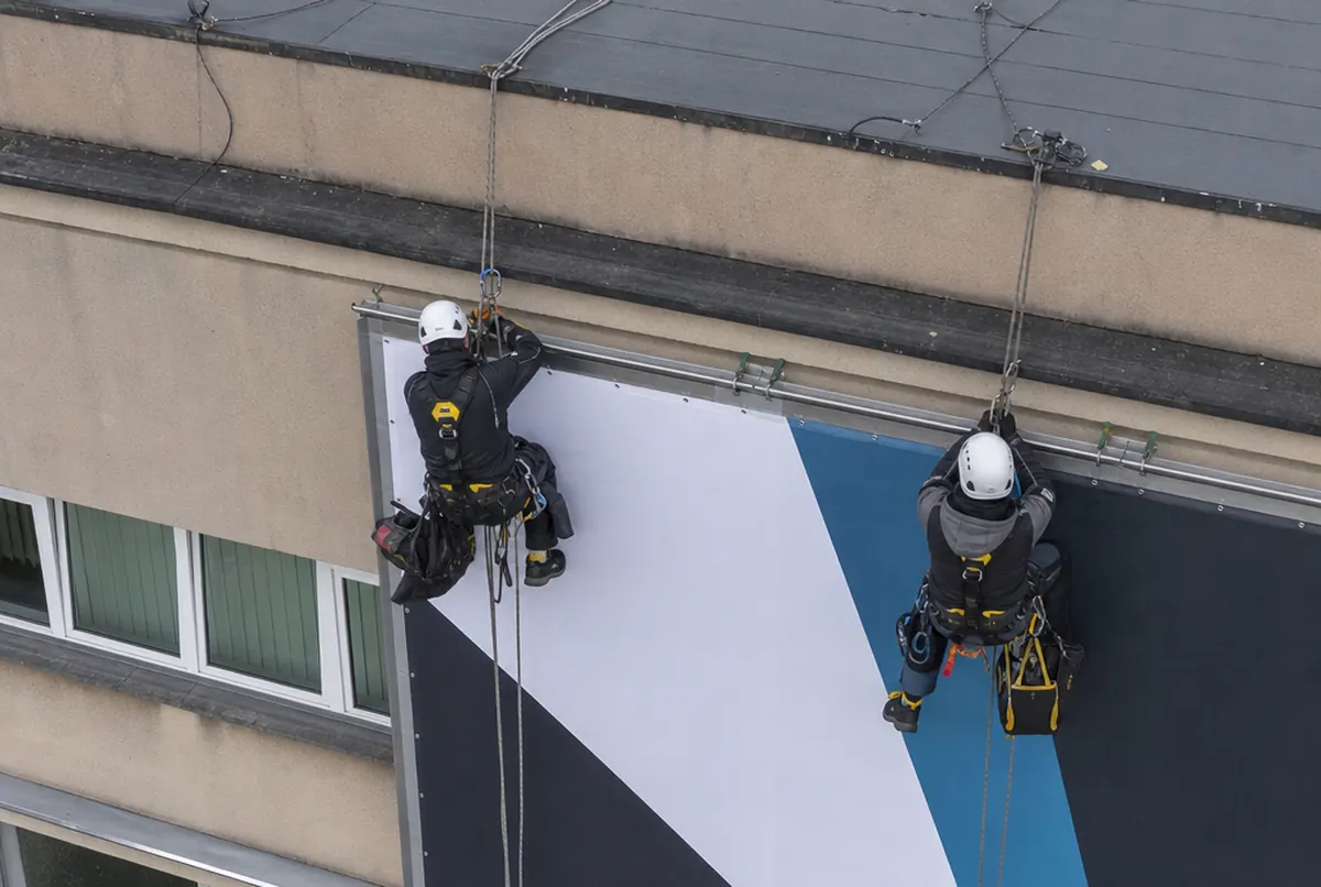 Alpiniści przemysłowi napinają baner na elewacji