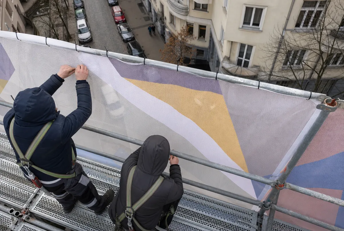 Monterzy na rusztowaniu przywiązują krawędź siatki mesh
