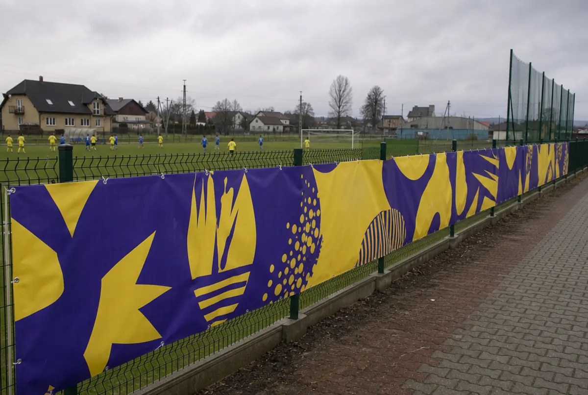 Frontlit banner with yellow and violet graphics stretched on a sports field mesh fence