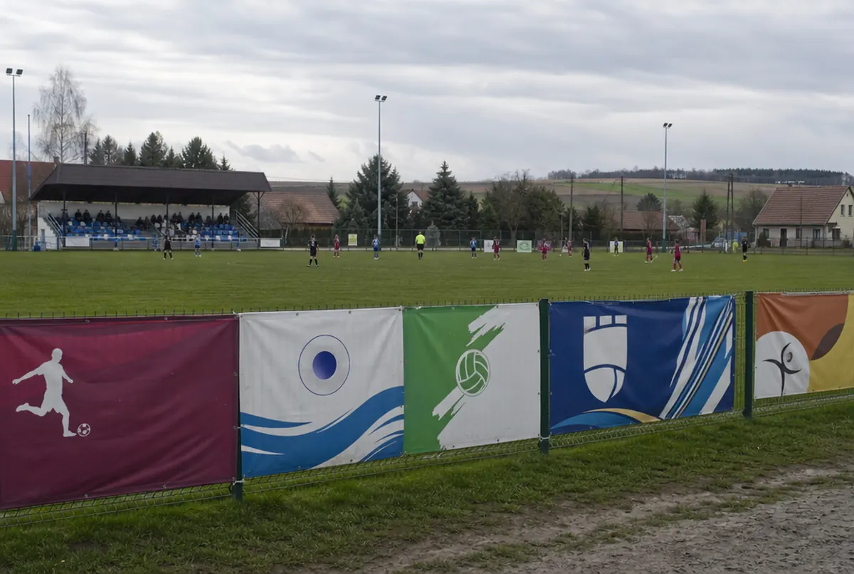 Row of sponsor banners on a football pitch fence during a youth match
