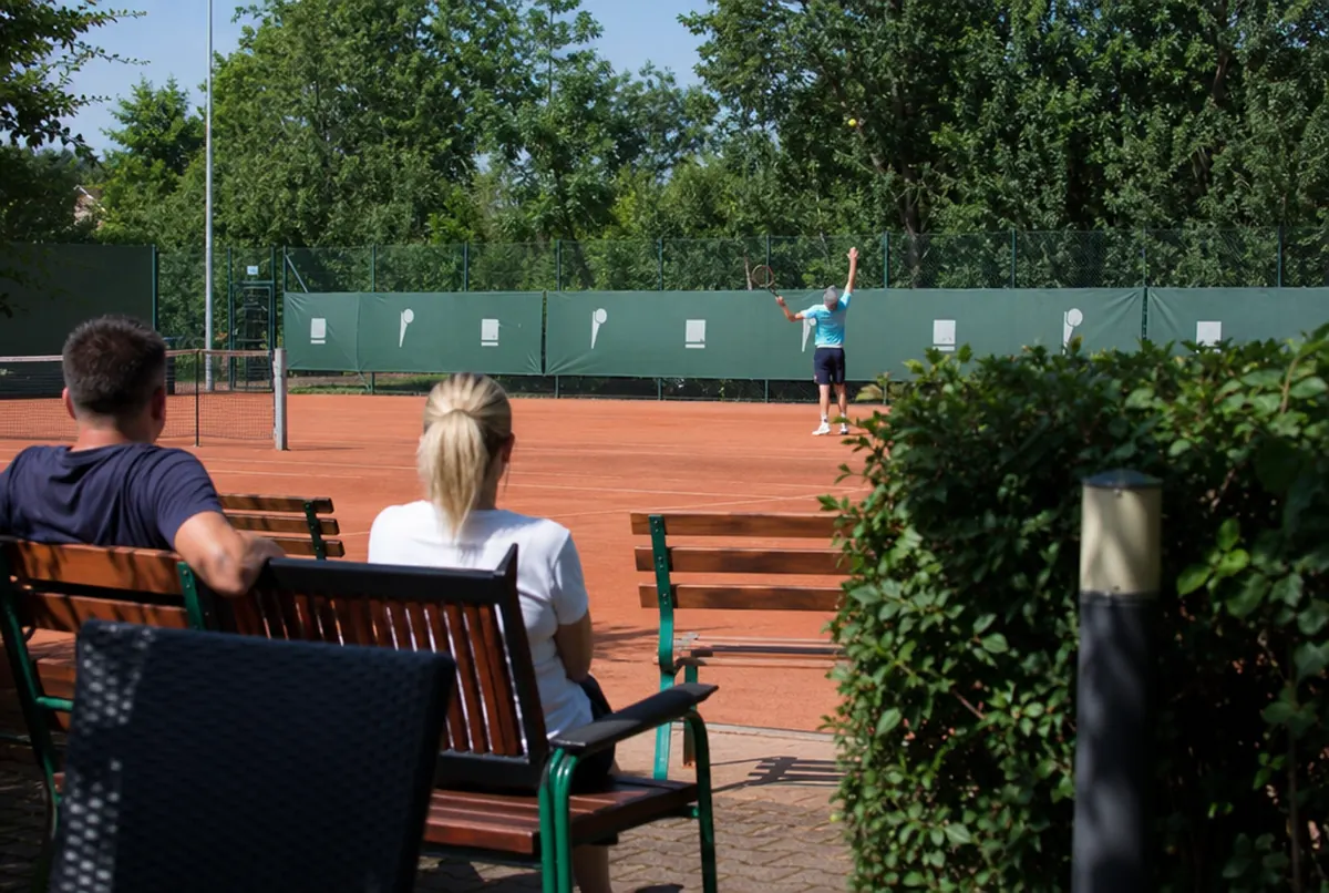 Dunkelgrüne bedruckte Blenden am Zaun eines Sandplatzes im Tennisclub