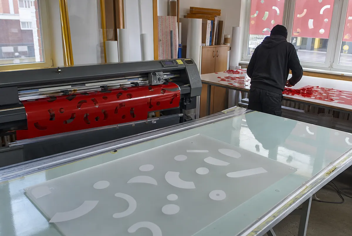 Plotter schneidet Formen aus roter Transluzentfolie, Mitarbeiter entgittert