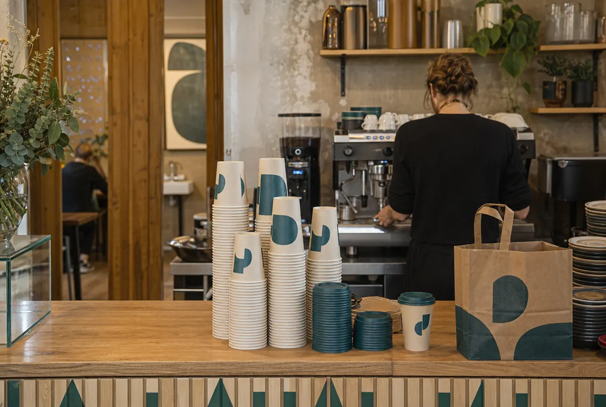 Bedruckte Pappbecher zum Mitnehmen auf der Café-Theke, Barista im Hintergrund