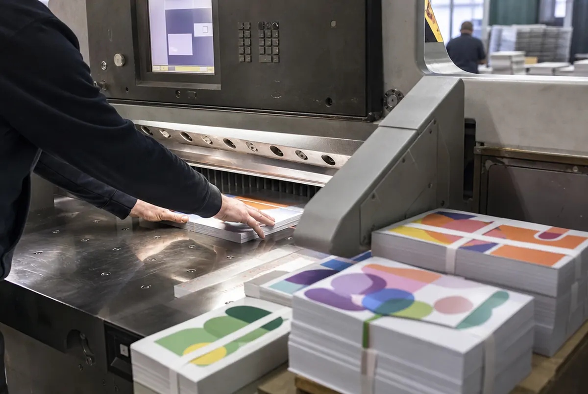 Massicot coupant une pile de planches de stickers, liasses finies à côté