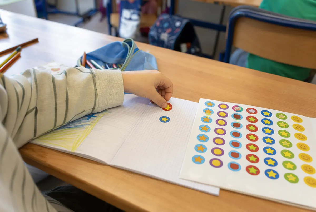 Main d'enfant collant un sticker récompense dans un cahier d'école