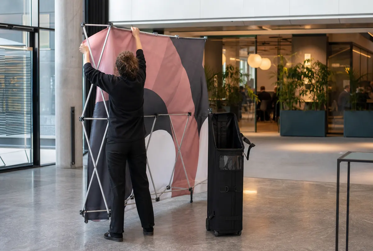 Aufklappen einer Hop-up-Wand mit Stoff neben der Rollentasche