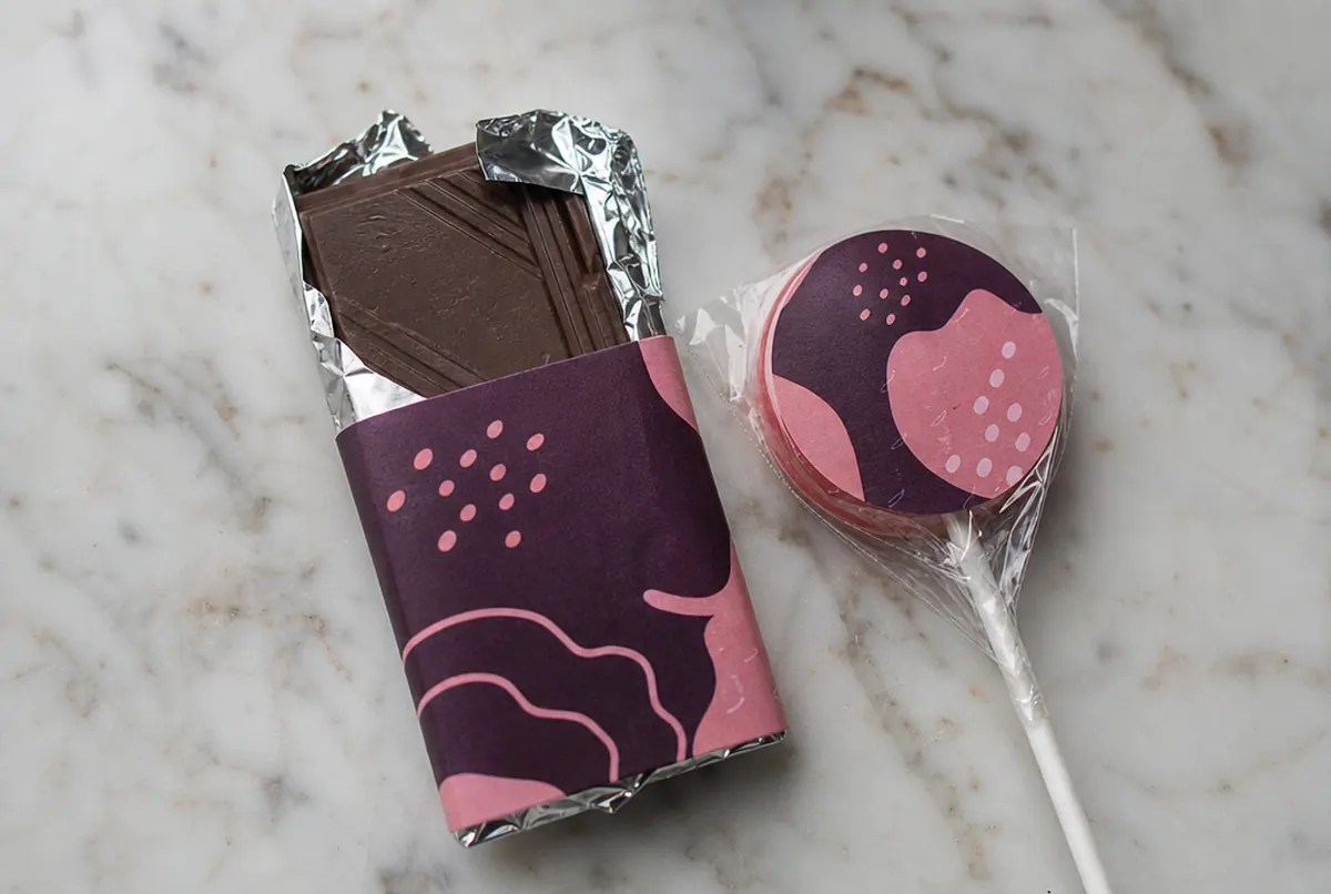 Nahaufnahme einer Mini-Schokolade mit bedruckter Banderole und eines Lollis mit Aufkleber