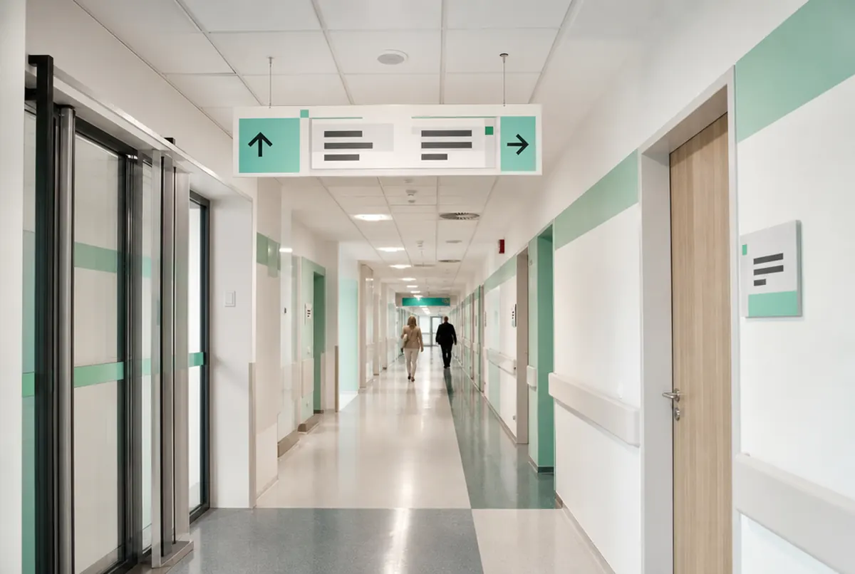 Einheitliches Leitsystem im Klinikflur: Hängeschild mit Pfeilen und mintgrüne Zonenstreifen